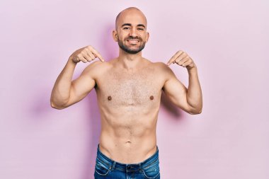 Genç kel adam üstsüz, kendine güvenen yüzünde bir gülümsemeyle kendini gururlu ve mutlu olarak gösteriyor.. 