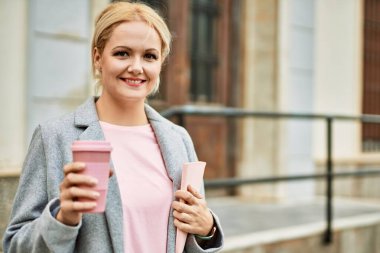 Genç sarışın iş kadını gülümseyerek şehirde kahve içiyor..