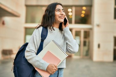 Genç ortadoğulu kız gülümsüyor. Şehirdeki akıllı telefondan konuşuyor..
