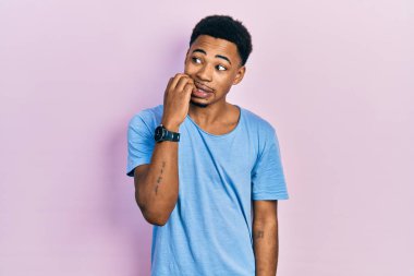 Genç Afro-Amerikalı bir adam, günlük mavi tişört giyiyor. Stresli ve gergin görünüyor. Ağzı tırnak yiyen elleri var. anksiyete. 