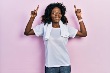 Genç Afro-Amerikan kadın spor giysisi ve havlu giyiyor. Şaşırmış, şaşırmış ve parmaklarıyla işaret ediyor ve kollarını kaldırıyor.. 