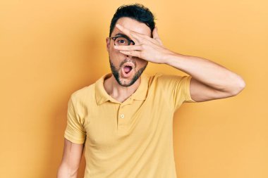 Günlük kıyafetler ve gözlük takan genç İspanyol adam şok içinde yüzünü ve gözlerini kapayarak utangaç ifadesiyle parmaklarından bakıyor.. 