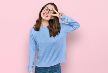 Gündelik giysiler ve gözlük takan genç güzel bir kadın barış sembolü yapıyor. Yüzünde parmaklar, gülümseyerek zaferi gösteriyor. 