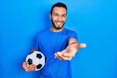 Sakallı, futbol topu tutan, neşeli gülümseyen, yardım eli uzatan ve kabul gören İspanyol bir adam.. 