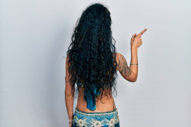 Bindi giyen ve geleneksel göbek dansı kıyafetleri giyen genç bir kadın parmak eliyle öne doğru poz veriyor. 