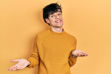 Yakışıklı hippi genç adam gündelik sarı süveter giyiyor. Neşeli gülümsüyor ve kollarını açıyor. Hoş geldin, olumlu ve kendinden emin selamlar. 