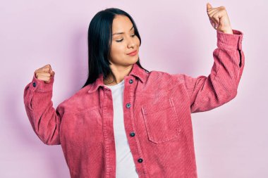 Burun piercingli, sıradan pembe ceket giyen güzel İspanyol kadın, gururla gülümseyen kol kaslarını gösteriyor. fitness konsepti. 