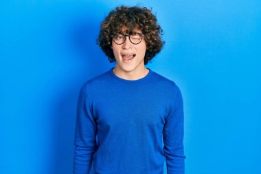 Yakışıklı, gündelik kıyafetler giyen ve gözlüklü genç adam kameraya seksi bir ifadeyle bakıyor, neşeli ve mutlu bir yüzle.. 