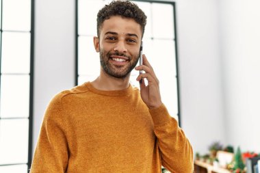 Genç Arap adam akıllı telefondan konuşuyor. Yılbaşı ağacının yanında duruyor..