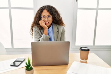 Ofiste masa başında oturan güzel İspanyol iş kadını dizüstü bilgisayarla çalışıyor. Ağzı tırnak ısıran elleri yüzünden gergin ve stresli görünüyor. anksiyete. 