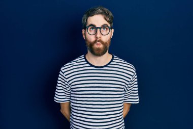 Sakallı, çizgili tişört ve gözlüklü beyaz bir adam dudağıyla balık suratı yapıyor, çılgınca ve komik bir jest. Komik ifade. 