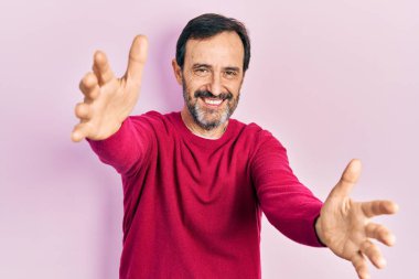 Orta yaşlı İspanyol bir adam sıradan kıyafetler giyip kameraya bakıyor. Sarılmak için kollarını açmış gülümsüyor. Mutluluğu kucaklayan neşeli bir ifade.. 