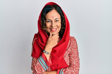 Orta yaşlı İspanyol kadın geleneksel Sherwani sari giysileri giyiyor kameraya kendinden emin bakıyor kollarını kavuşturmuş ve çenesini kaldırmış gülümsüyor. Olumlu düşünmek. 