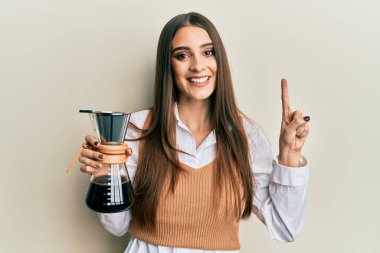 Güzel esmer, elinde çözünür kahve makinesi olan genç bir kadın bir fikir veya soruyla gülümsüyor ve mutlu bir yüzle işaret ediyor. 