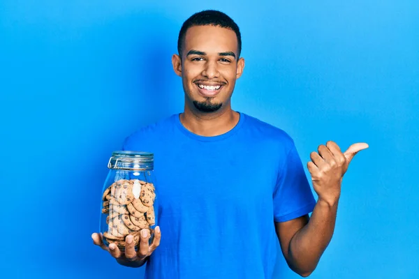 Joven Afroamericano Hombre Sosteniendo Tarro Galletas Chispas Chocolate Apuntando Pulgar — Foto de Stock