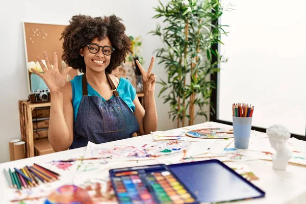 在艺术演播室里 一个美丽的非洲裔美国女人 带着非洲式的发型 带着自信和快乐的笑容 用七号手指指指着 — 图库照片