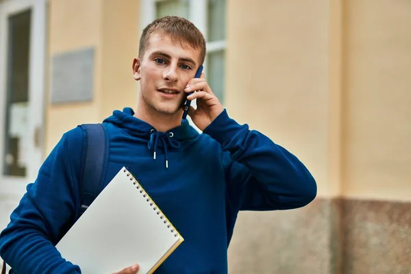 Νεαρή Ξανθιά Φοιτήτρια Μιλάει Στο Smartphone Κρατώντας Σημειωματάριο Στο Πανεπιστήμιο — Φωτογραφία Αρχείου