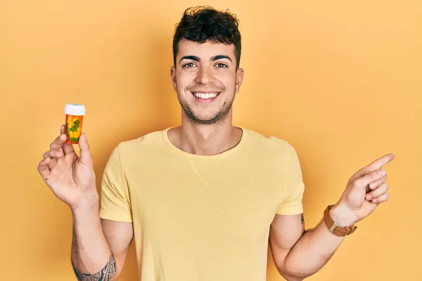 Молодий Іспаномовний Чоловік Тримає Таблетки Посміхаючись Щасливим Вказуючи Рукою Пальцем — стокове фото