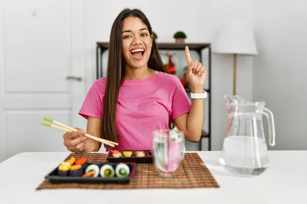 若いですブルネット女性食べる寿司箸を使用して笑顔と驚きと指で指摘し 腕を上げ — ストック写真