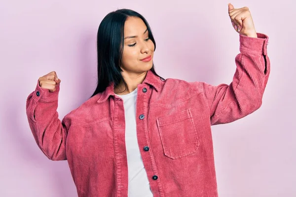 Burun piercingli, sıradan pembe ceket giyen güzel İspanyol kadın, gururla gülümseyen kol kaslarını gösteriyor. fitness konsepti. 