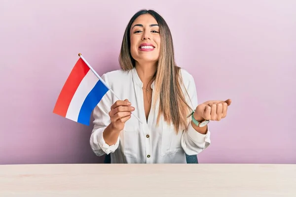 Jovem Hispânica Segurando Bandeira Holandesa Sentada Mesa Gritando Orgulhoso Celebrando — Fotografia de Stock