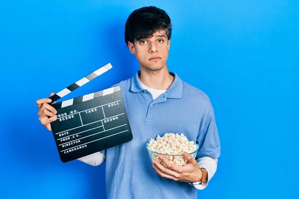 Przystojny Hipsterski Młody Człowiek Jedzący Popcorn Trzymający Kinową Klapkę Zrelaksowany — Zdjęcie stockowe