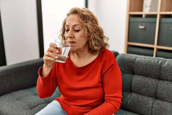 Biała Kobieta Średnim Wieku Pije Wodę Siedząc Kanapie Domu — Zdjęcie stockowe