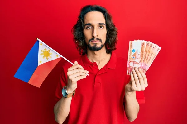 Young Hispanic Man Holding Philippines Flag Pesos Banknotes Relaxed Serious — Stock Photo, Image