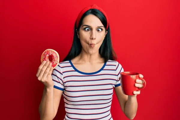 Young Hispanic Woman Eating Doughnut Drinking Coffee Making Fish Face — Stock Photo, Image