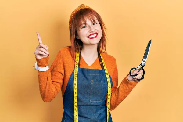 Pelirroja Joven Modista Diseñadora Usando Delantal Atelier Sosteniendo Tijeras Sonriendo — Foto de Stock