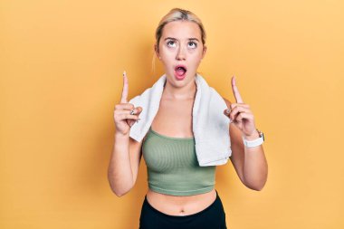 Spor kıyafetleri ve havlu giyen genç sarışın kız hayret ve şaşkınlık içinde yukarı baktı ve parmaklarıyla işaret etti ve kollarını kaldırdı.. 