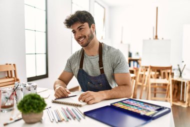 Sanat stüdyosundaki genç İspanyol adam yüzünde gülümseme ve doğal ifadeyle yan yana bakıyor. Kendinden emin gülen. 