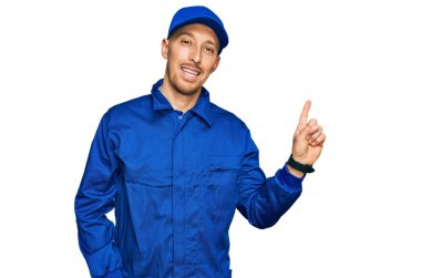 Sakallı, inşaatçı tulumu giyen, yüzünde kocaman bir gülümseme olan, eli kameraya bakan kel bir adam.. 