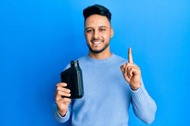 Motor yağı şişesi tutan genç Arap bir fikir veya soruyla gülümseyen mutlu bir yüzle işaret eden bir numara. 