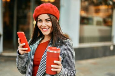 Genç İspanyol kadın akıllı telefon kullanıyor ve şehirde kahve içiyor..