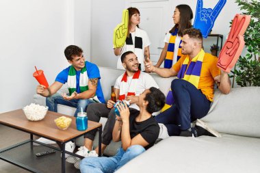 Evde futbol maçı izleyen ve destekleyen bir grup genç arkadaş..