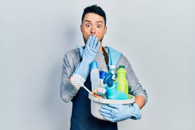 Genç İspanyol adam temizleme ürünlerini elinde tutuyor. Ağzını eliyle kapatıyor. Şok geçiriyor ve hata yapmaktan korkuyor. şaşırmış ifade 