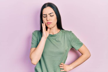 Mavi gözlü güzel bir kadın diş ağrısından ya da diş ağrısından dolayı elleri ağızlarına değen sıradan bir tişört giyiyor. dişçi 