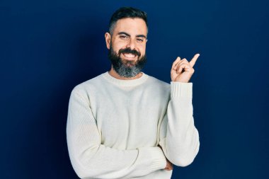 Yüzünde kocaman bir gülümseme olan, gündelik kıyafetler giyen genç İspanyol adam, kameraya el ve parmak ile bakıyor.. 