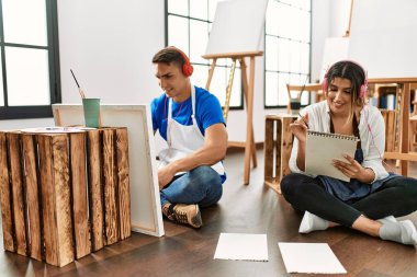 Sanat okulunda iki öğrenci kulaklık takıp resim yaparken mutlu bir şekilde gülümsüyor..