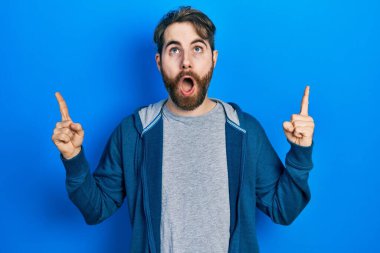 Sıradan bir kazak giyen beyaz bir adam şaşkın şaşkın yukarı bakıyor ve parmaklarıyla işaret ediyor ve kolunu kaldırıyor.. 