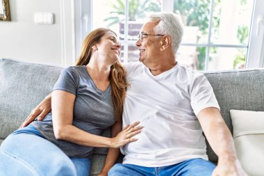 Orta yaşlı İspanyol çift mutlu bir şekilde gülümsüyor ve evdeki kanepede oturup sarılıyorlar..