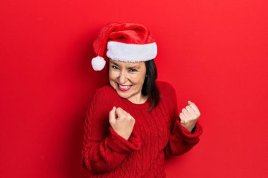 Orta yaşlı İspanyol kadın Noel şapkası takıyor. Kolları havada ve gözleri kapalı zaferi kutluyor. Kazanan konsept. 