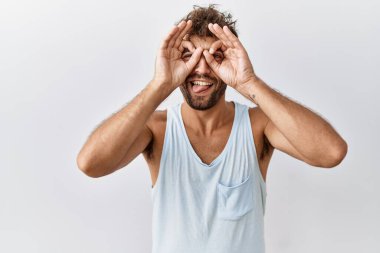 Tecrit edilmiş arka planda duran yakışıklı genç adam dürbün gibi jest yapıyor. Dürbün dilini çıkarıyor, gözler parmaklarından bakıyor. Çılgın ifade. 