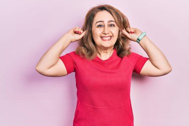 Orta yaşlı beyaz kadın günlük kıyafetler giyip gülümsüyor kulakları parmaklarıyla çekiyor, komik bir jest. deneme sorunu 