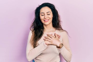 Gündelik kıyafetler giyen genç İspanyol kadın elleri göğsünde gülümsüyor, gözleri kapalı, yüzünde minnet ifadesi var. sağlık kavramı. 