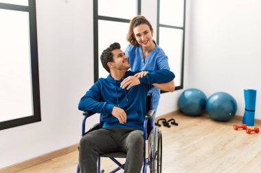 Genç engelli adam klinikte tekerlekli sandalyede oturarak hareket egzersizi yapıyor..