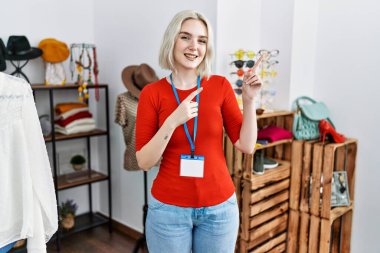 Kafkasyalı genç bir kadın perakende mağazasında yönetici olarak çalışıyor gülümsüyor ve kameraya bakıyor iki eliyle ve parmaklarıyla kenarı işaret ediyor.. 