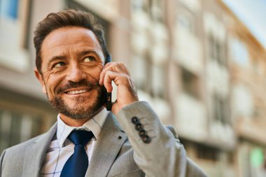 Orta yaşlı işadamı gülümsüyor. Şehirdeki akıllı telefondan konuşuyor..