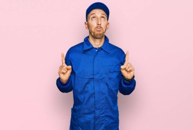 Kel, sakallı, inşaatçı tulumu giyen, üzgün ve üzgün görünen, parmaklarıyla yön gösteren mutsuz ve depresif bir adam.. 